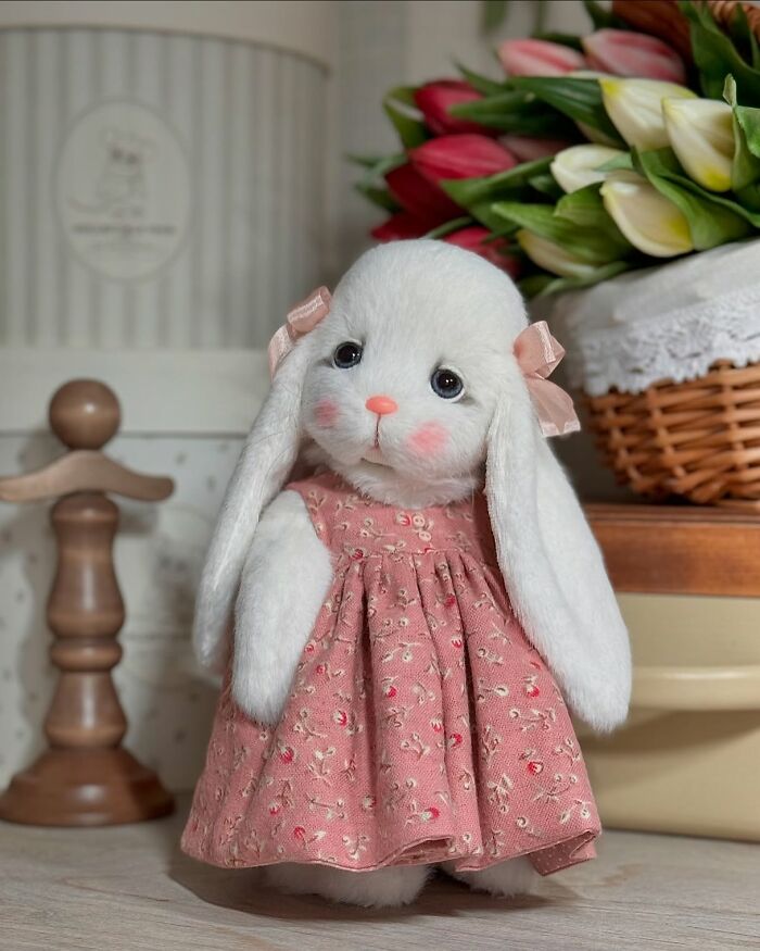 Whimsical plush toy bunny in a floral dress, crafted with intricate handmade details, standing beside a basket of flowers.