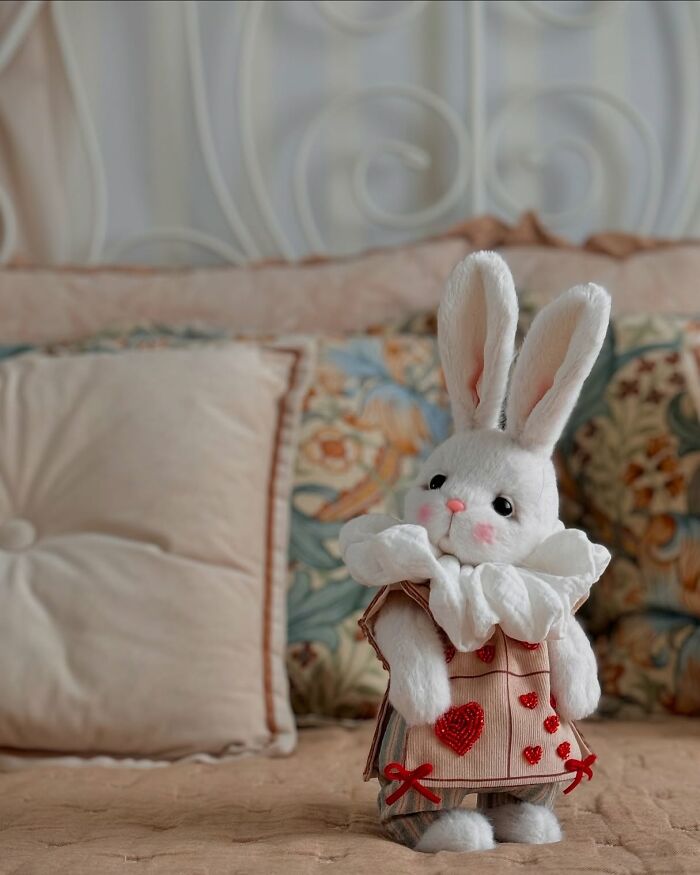Whimsical handmade plush rabbit toy with heart details, set on a cozy bed with pillows in the background.