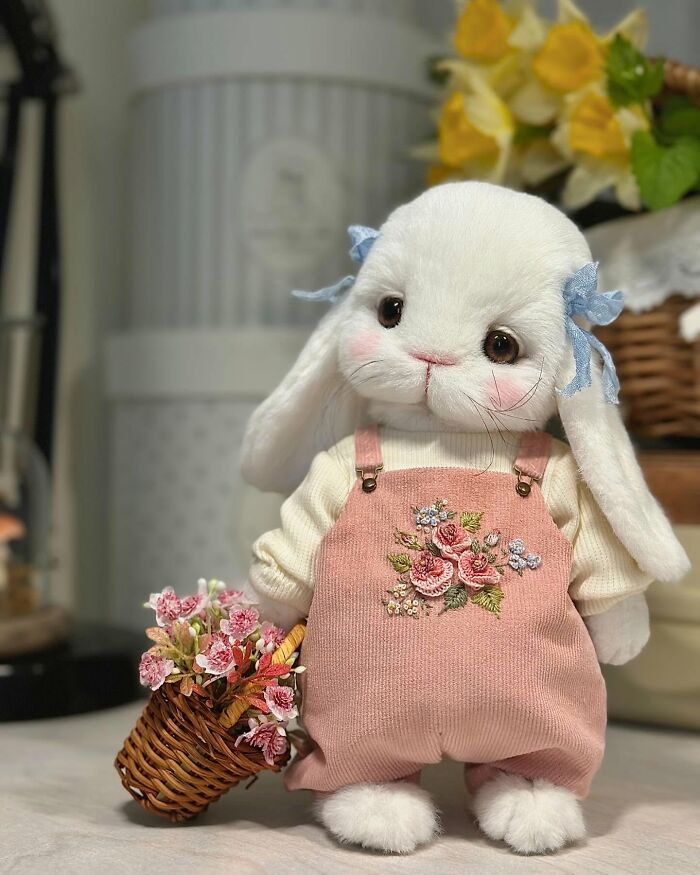 Whimsical plush toy rabbit in pink overalls holding a basket of flowers, showcasing handmade artistry.
