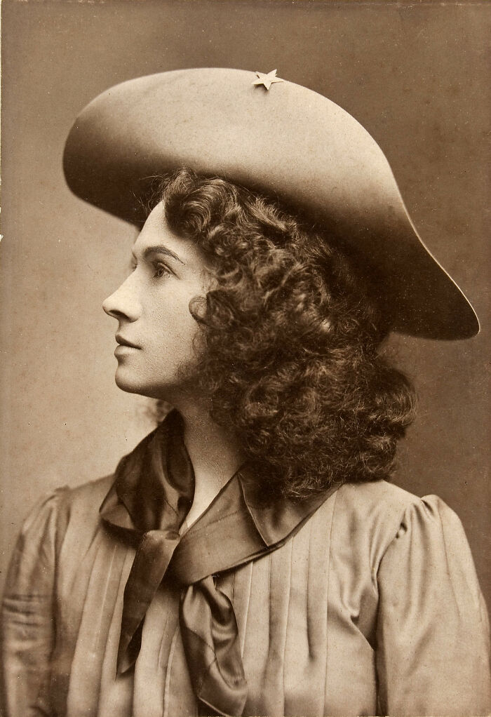 Sepia-toned rare photo of a famous historical figure woman with curly hair wearing a wide-brimmed hat and vintage attire.