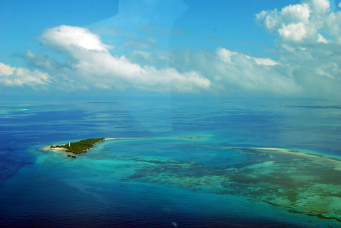 Aerial view of incredible coastal vista with a small island surrounded by turquoise waters and blue sky.