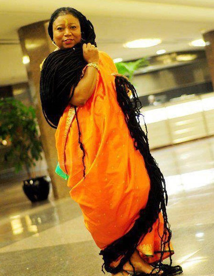 Person in an orange outfit showcasing real-life superpowers with extremely long hair indoors.