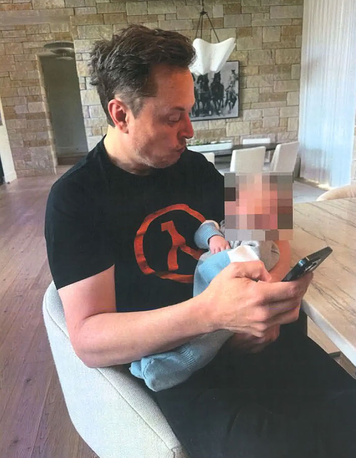 Man holding a baby, wearing a black shirt with red logo, using a smartphone in a modern living room setting. Man holding a baby, wearing a black shirt with red logo, using a smartphone in a modern living room setting.