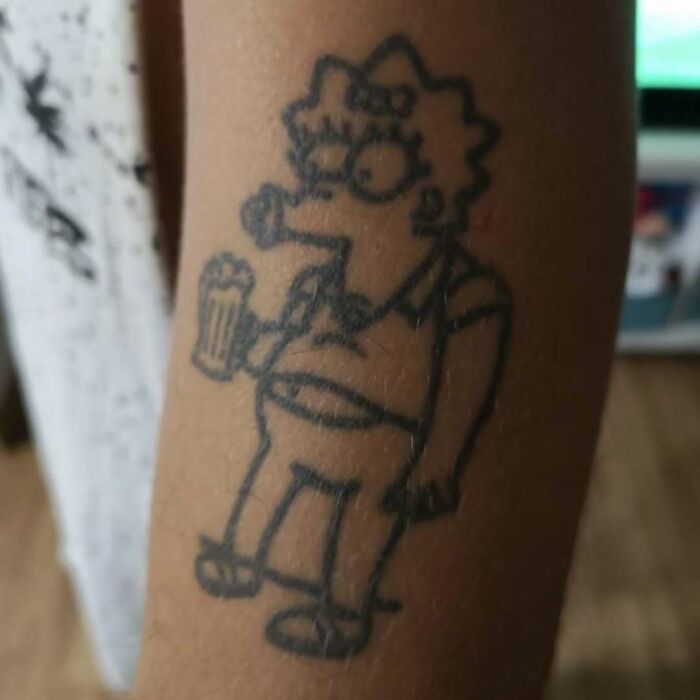 Simpsons tattoo featuring a distorted character holding a beer on an arm.