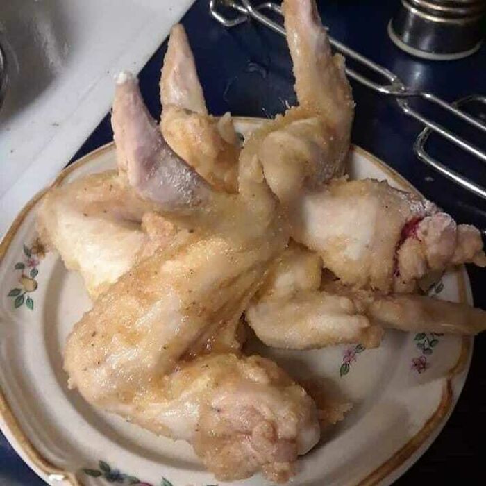 Unappetizing chicken wings on a floral plate, slightly breaded and uncooked, presented on a kitchen counter.