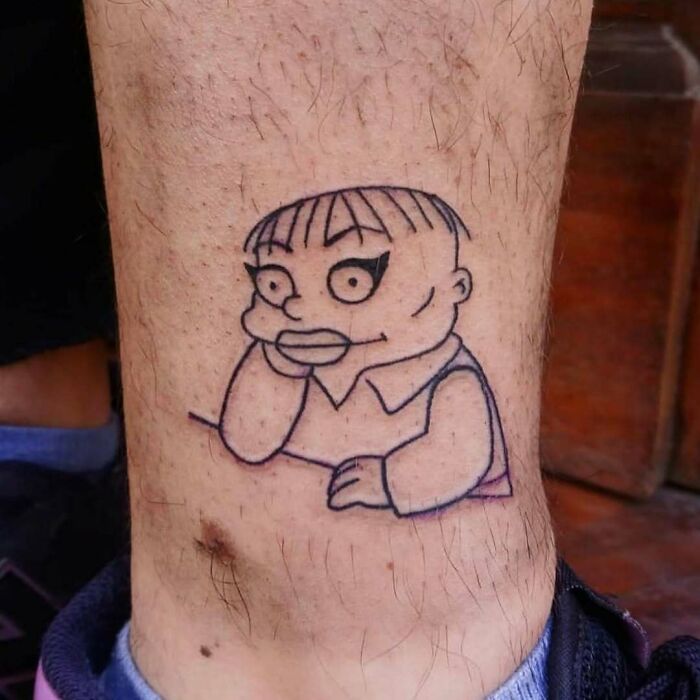 A black line tattoo of a Simpsons character on a person's leg.
