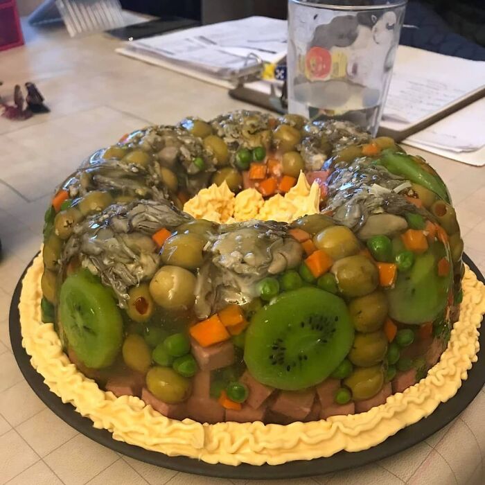 Unappetizing food photo with jelly mold containing olives, peas, and kiwi, styled with cream on a table.