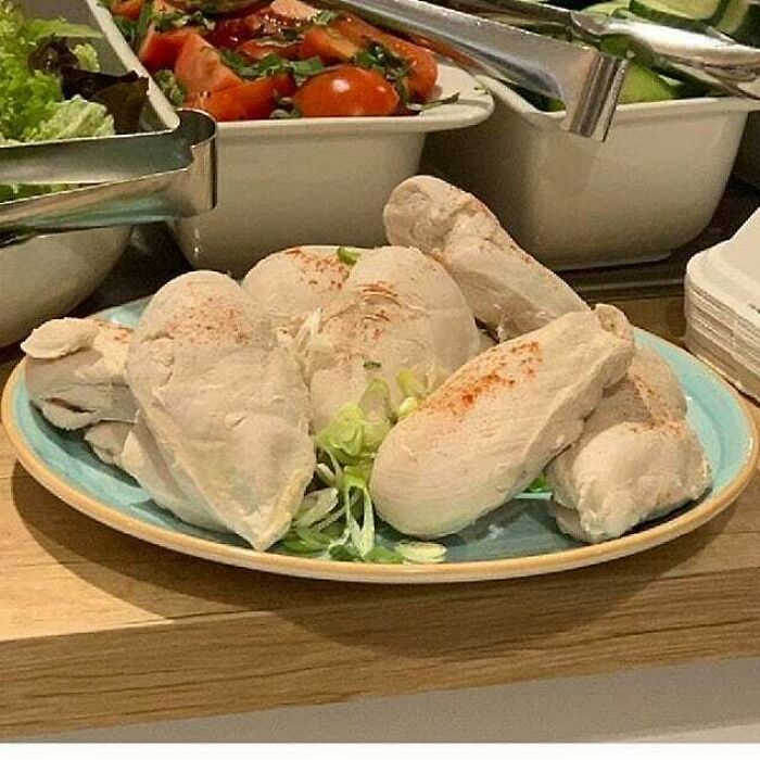 Plate of unappetizing chicken garnished with scallions, alongside fresh salad bowls.