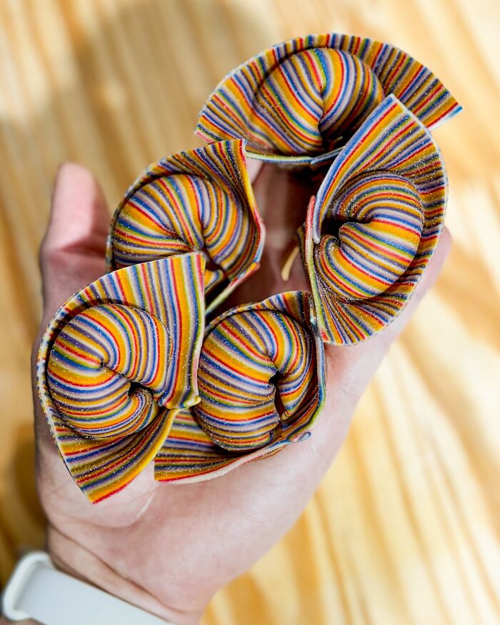Handcrafted pasta with colorful stripes held in a hand, showcasing artistic patterns by a culinary artist chef.