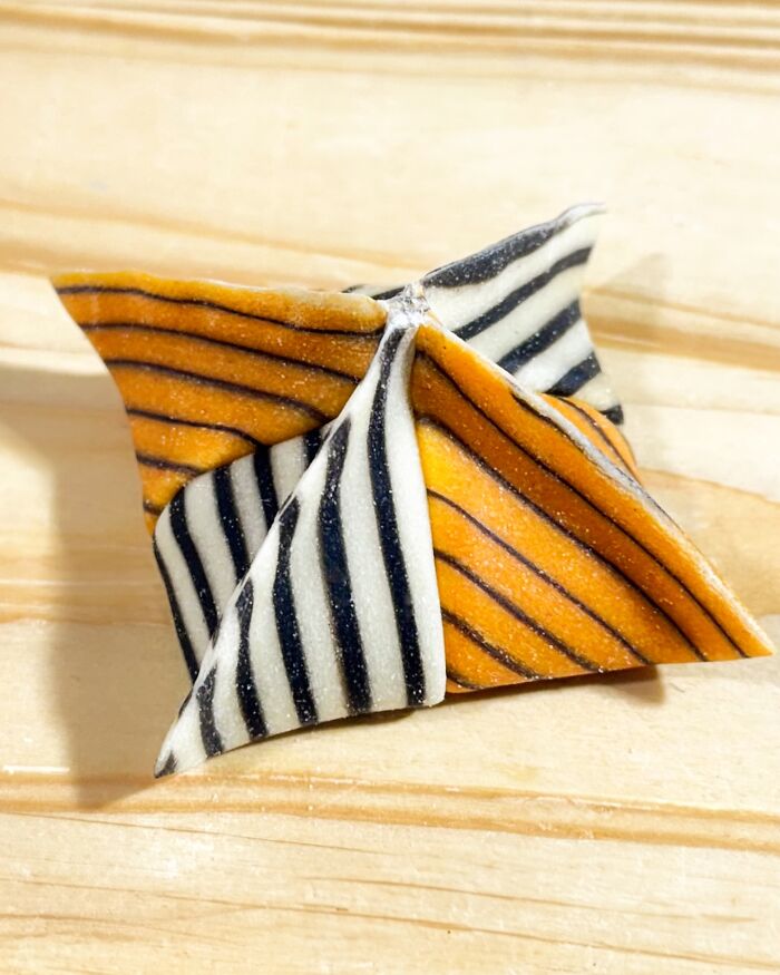 Colorful handcrafted pasta with orange and black stripes on a wooden surface, showcasing culinary artistry.