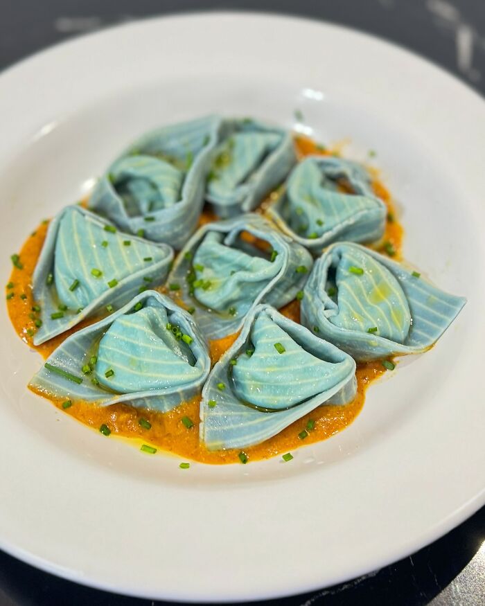 Colorful handcrafted pasta with blue hues and intricate patterns on a white plate, showcasing culinary artistry.