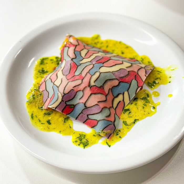 Colorful handcrafted pasta with intricate patterns, served on a white plate with vibrant yellow sauce.
