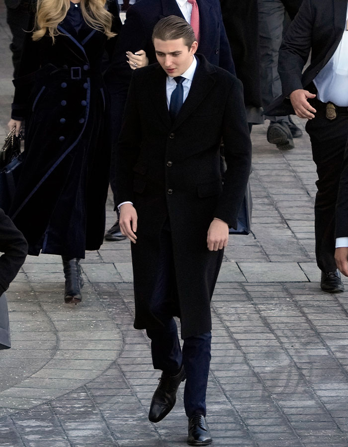 Young man in a formal coat walking with Secret Service agents for safety at college freshman year.