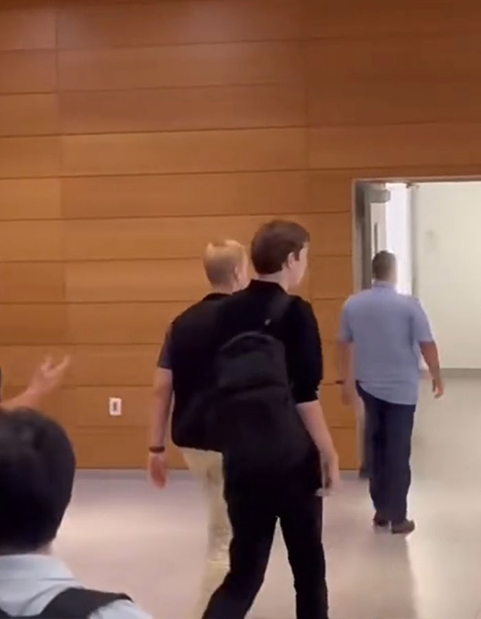 Person with a backpack in a college hallway escorted by another person, illustrating Secret Service safety methods.