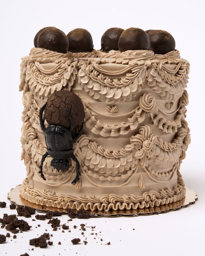 Intricately decorated vegan cake with icing patterns and a realistic bug design on the side.