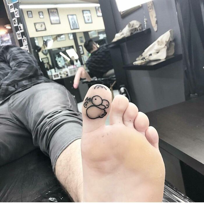 Toe tattoo of a cartoon character in a tattoo parlor, highlighting quirky Simpsons tattoo design.