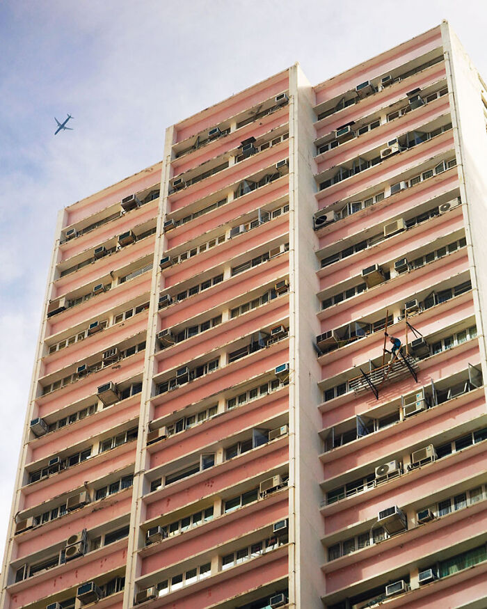 Below The Passing Plane, 2024 - A Scaffolder Is Grabbing A Bamboo Pole On The Facade Of A Building