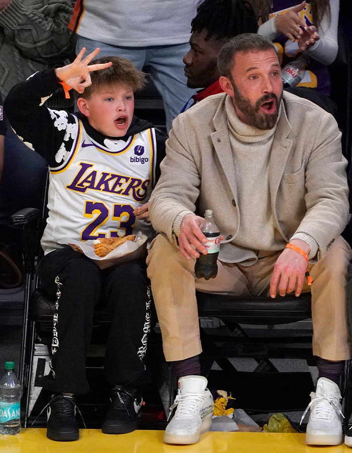 Man with beard and child in Lakers jersey at basketball game, promoting work ethics in rich kids.