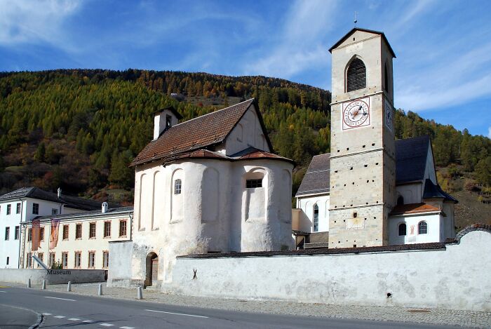 Historic church and clock tower against a forested hillside, showcasing architectural wonders in a serene setting.