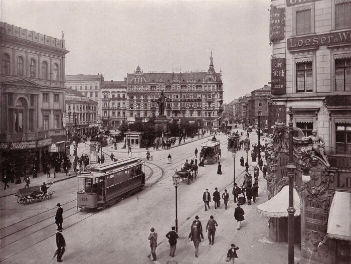 Busy European city street scene with trams, pedestrians, and historic buildings showing life in Europe 100 years ago.