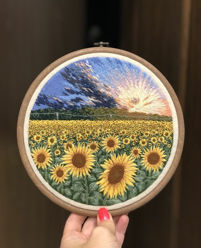 Hand holding hoop with embroidery of sunflowers and a vibrant sunset.
