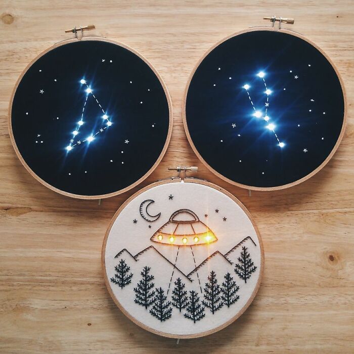 Embroidery of constellations and a UFO scene on wooden hoops, showcasing intricate artwork.