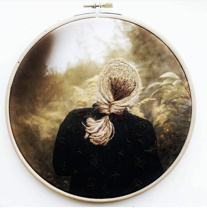 Embroidery artwork of a person with a woven braid walking in nature, captured in a circular hoop.