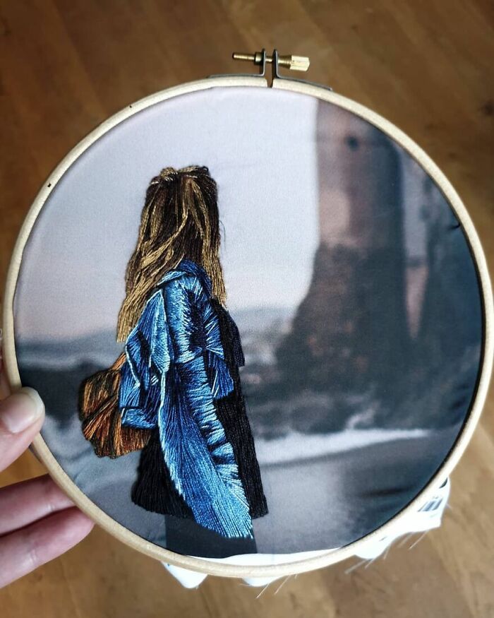 Embroidery artwork in a hoop depicting a figure in a blue coat with a blurred background.