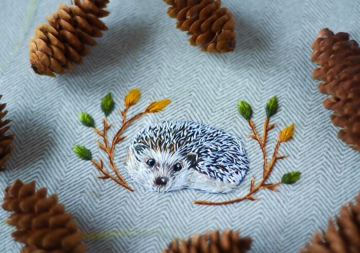 Embroidery of a hedgehog with leaves, surrounded by pine cones on fabric.