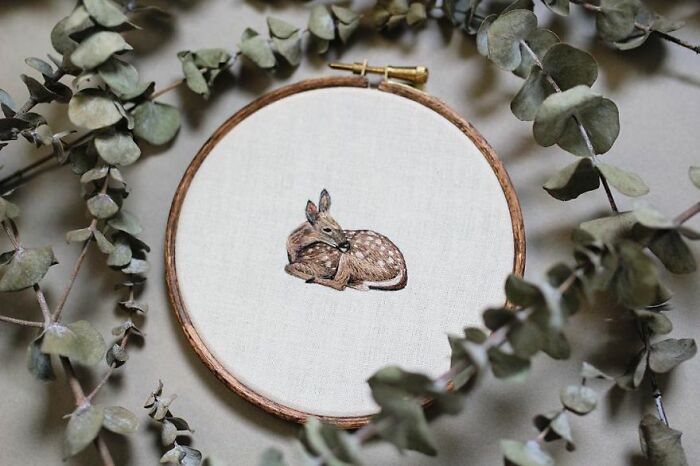 Embroidery of a resting fawn in a hoop surrounded by eucalyptus leaves.