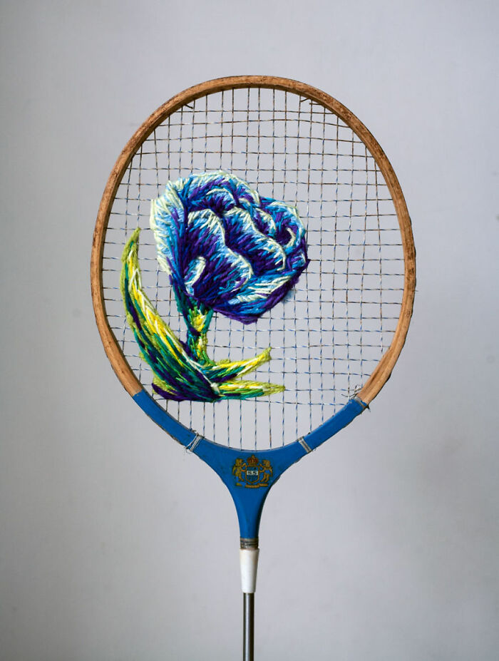Embroidery artwork of a blue flower on a vintage tennis racket.
