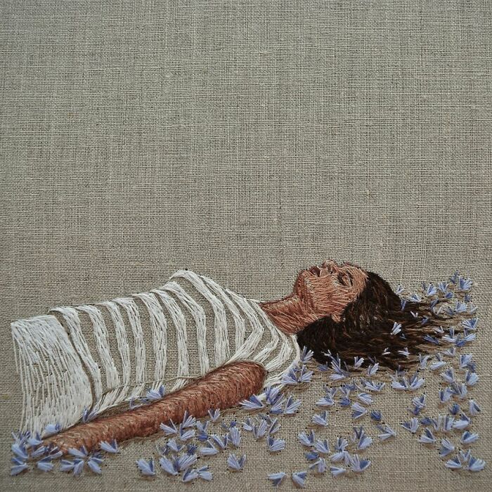 Embroidery artwork of a person lying in blue flowers on fabric, showcasing incredible needlework.