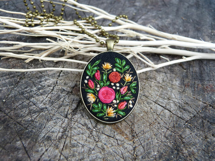 Oval pendant with vibrant floral embroidery, featuring pink and yellow flowers, displayed on a textured background.