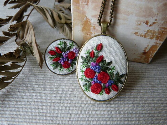 Embroidery jewelry with red and purple floral designs displayed on a textured surface.