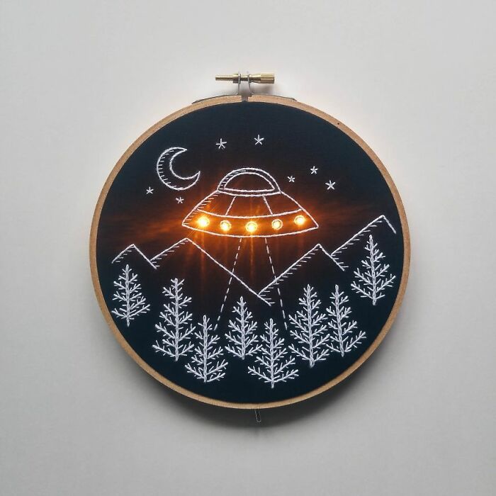 Embroidery art featuring a UFO, stars, and trees on a black fabric with glowing details.