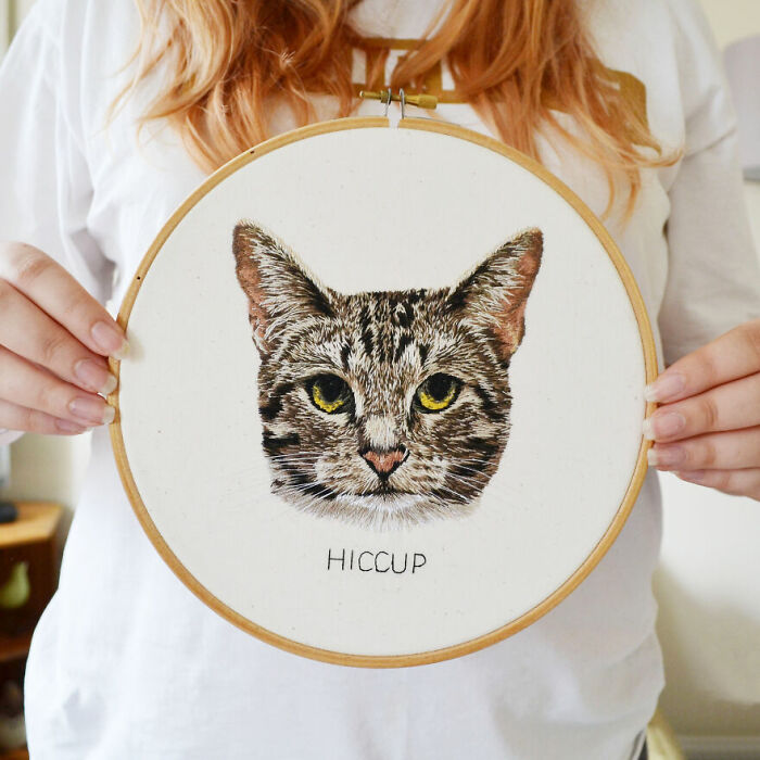 Person holding an embroidery of a cat's face titled "Hiccup" from Bored Panda community.