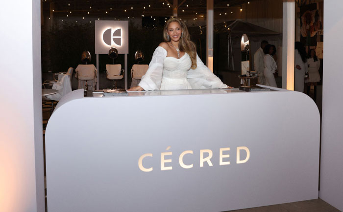 Beyonc&eacute; in a white dress at a branded C&eacute;cred counter, illustrating wealth-building in the arts.