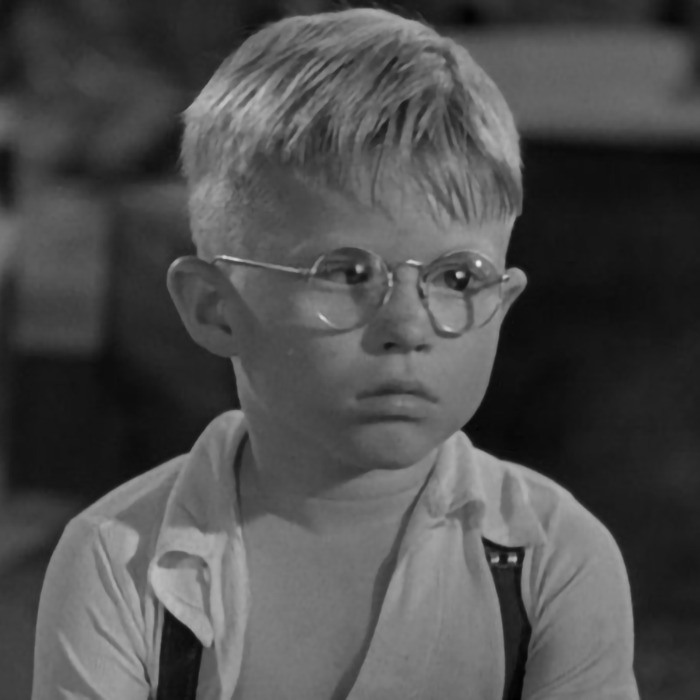 Young child actor wearing glasses, looking serious, in a black and white scene.