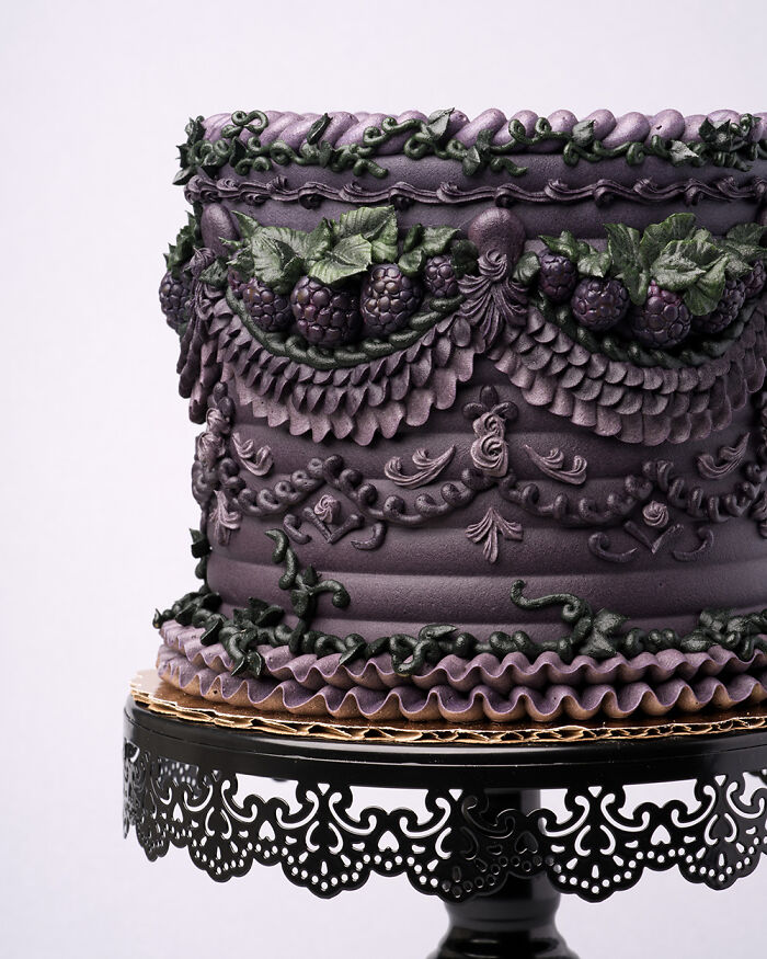 Vegan cake with intricate bug-inspired decorations, featuring dark purple icing and green leaf accents, on an ornate stand.