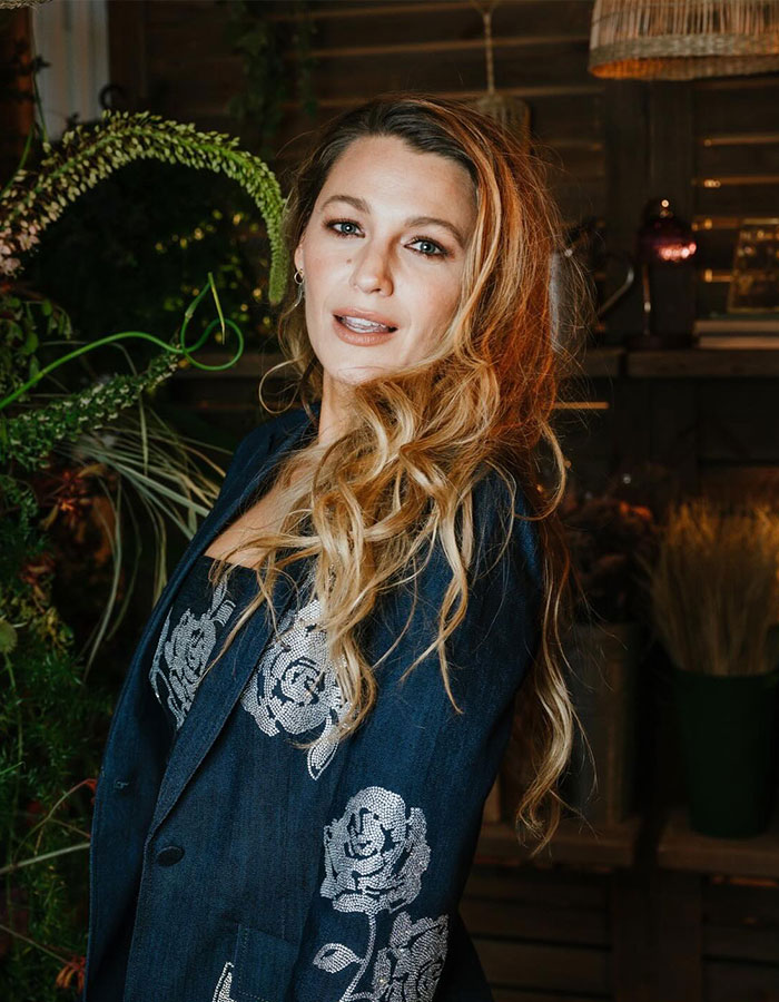 Woman wearing a floral patterned jacket, standing amid greenery.