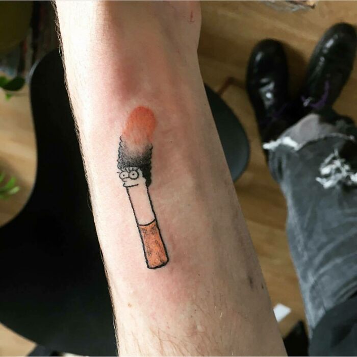 Tattoo of a matchstick resembling a character from The Simpsons on a person's arm.