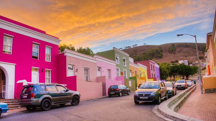 Colorful city street with vibrant houses under a dramatic sunset sky, resembling a real-life painting.