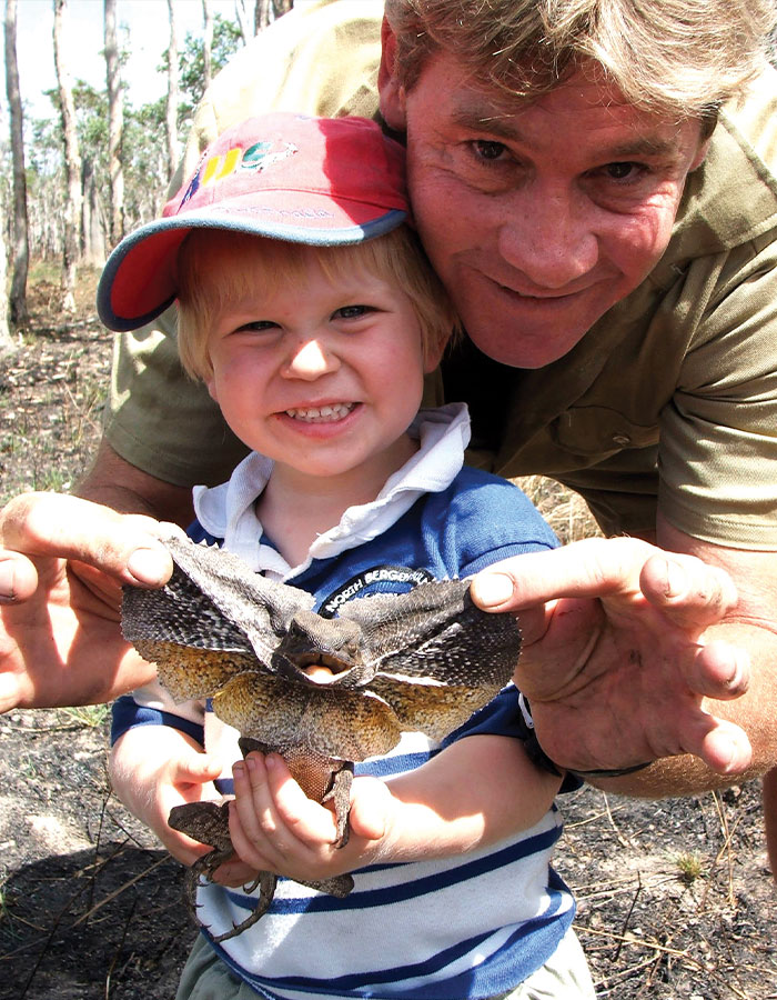 Father and son outdoors holding a frill-necked lizard, showing interest in wildlife exploration.