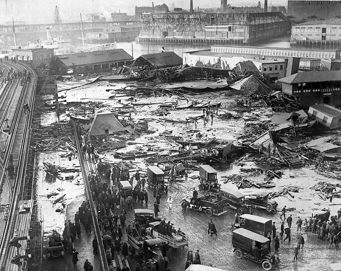 Historical scene after Boston Molasses Disaster, with debris, vehicles, and crowds gathered in the aftermath.