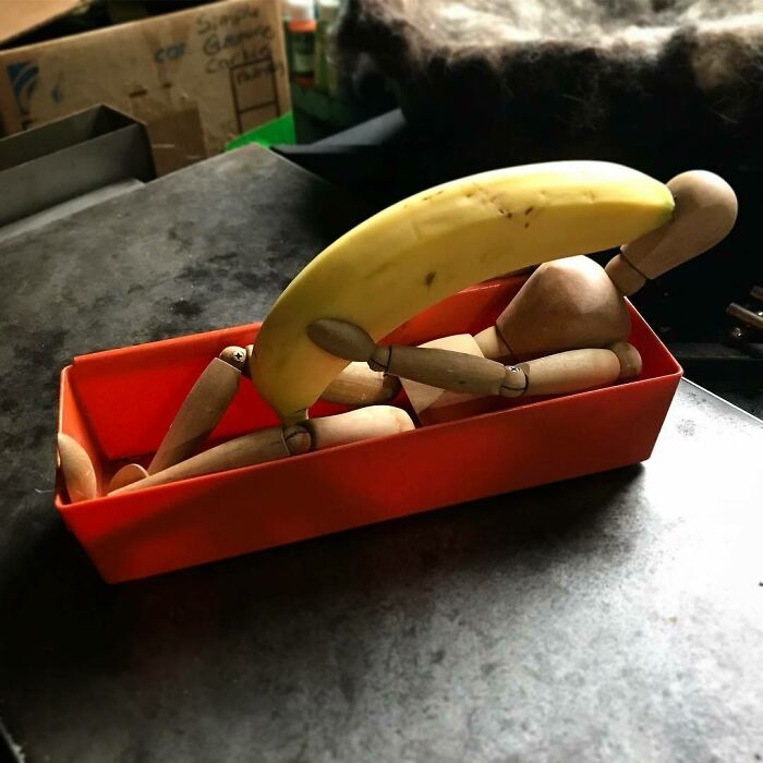 A wooden mannequin humorously posed with a banana in a red box, embodying hilarious moments.