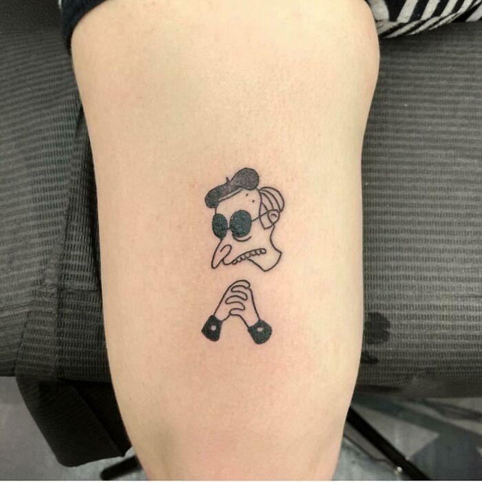 Minimalist Simpsons tattoo depicting a quirky character in sunglasses inked on forearm.
