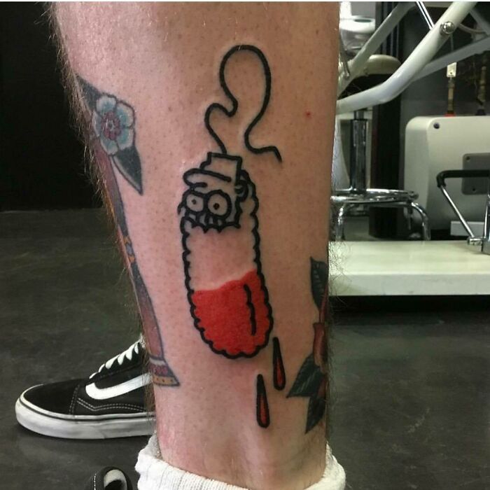 Simpsons tattoo of a cartoon character in a pickle costume on a person's leg in a tattoo studio.