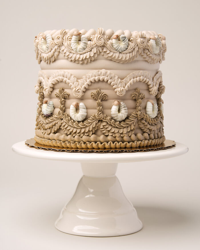 Intricately decorated cake with bug-themed icing on a white stand.