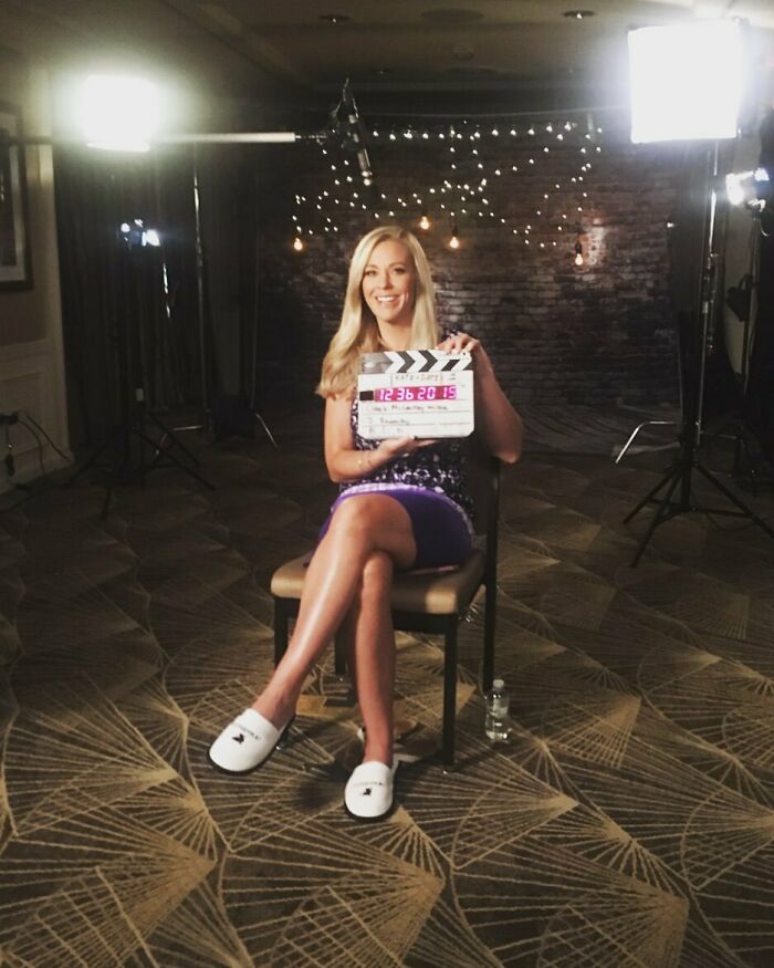 Woman holding film clapperboard sitting on chair in studio lighting setup for celebrity encounters interview session.