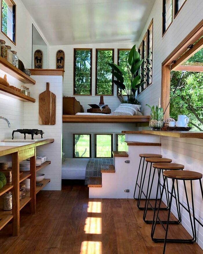 Cozy and modern tiny home interior with wooden floors, large windows, built-in seating, and natural light showcasing life off the grid.
